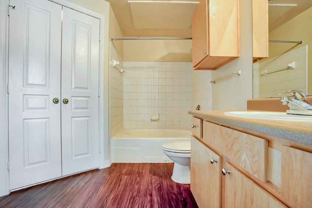 A bathroom with wood floor and plenty of cabinets and double doors and bathtub/shower and sink
