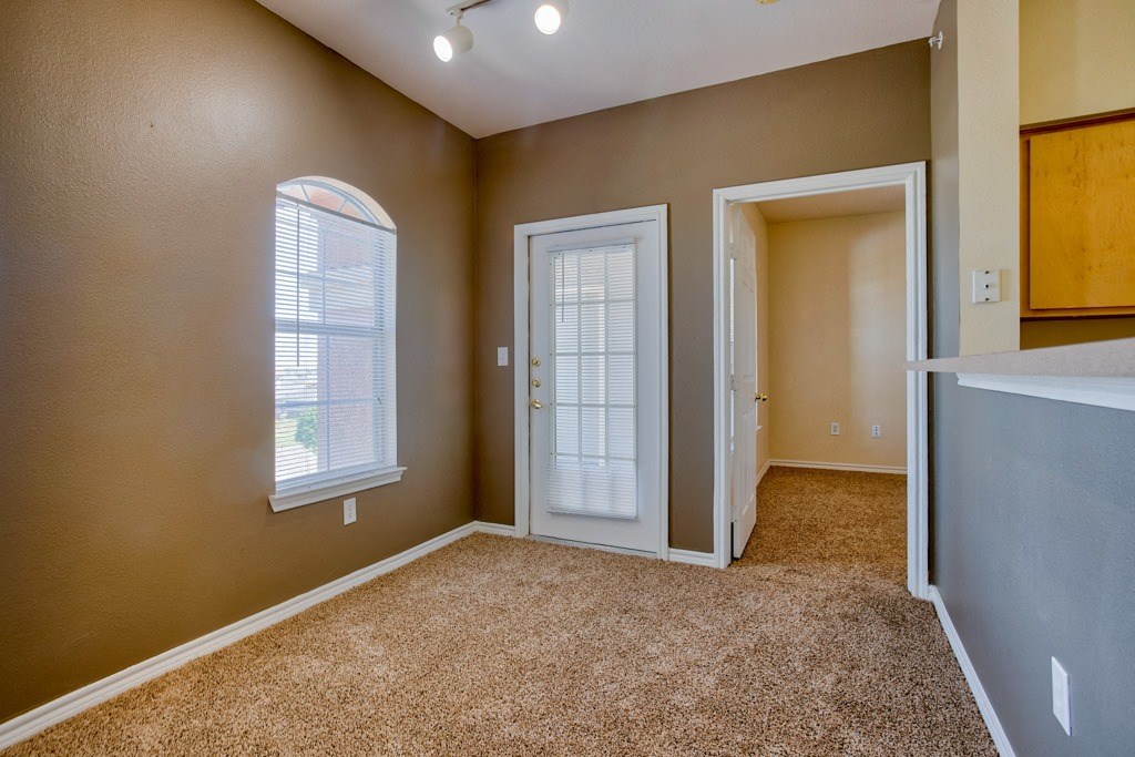 an empty living room with carpet and with an open door and a window with blinds