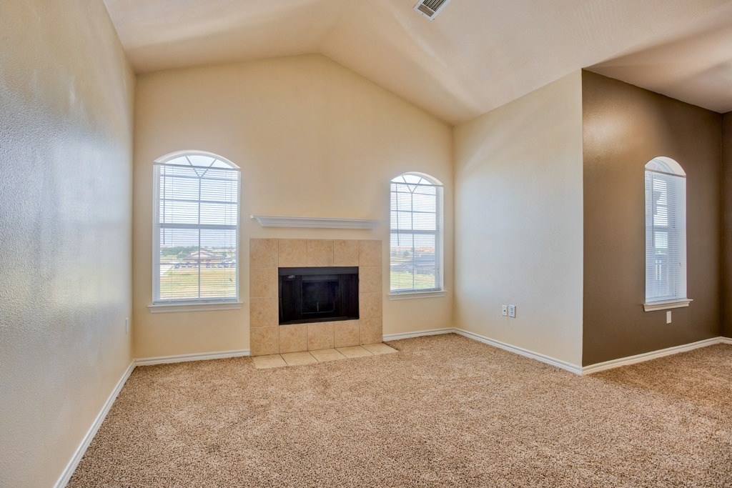 An empty living room with vaulted ceilings and fire pit and carpet and windows with blinds