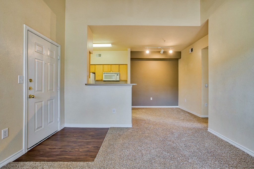 Empty Living room with carpet and wood floor entrance and kitchen in background