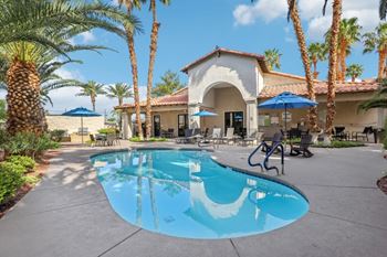 A pool surrounded by palm trees and a building in the background.