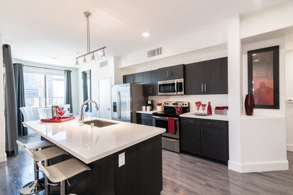 A kitchen with a ceiling light and stools and island and oven and microwave and stove and window and fridge