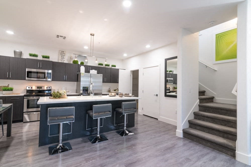 A kitchen with staircase and stools and island and ceiling lights and fridge and oven and microwave and stove