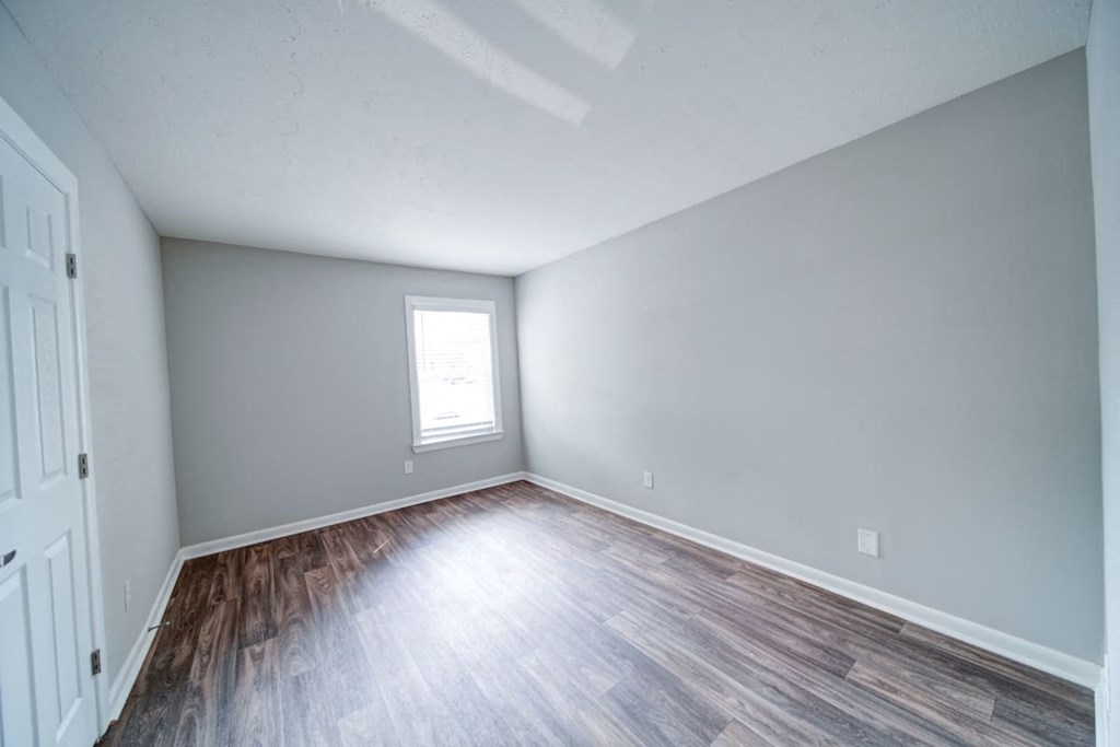an empty bedroom with hardwood floors and a window