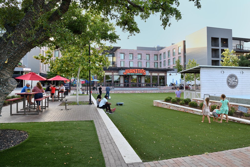 A group of people are sitting and standing on a grassy area in front of a building with a sign that says "JUANITAS".
