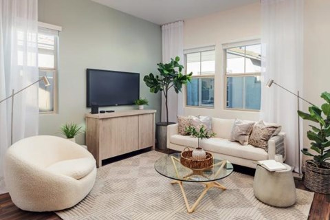 A living room with a white couch, a white chair, a glass coffee table, and a television on a cabinet.