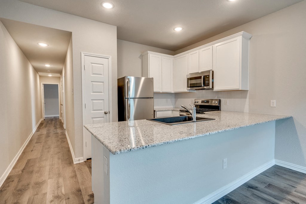 Apartments In Forth Worth For Rent - Cottages at Summer Creek - Kitchen with Wood-Style Flooring, Stainless Steel Appliances, White Cabinets, Pantry, Built-In Microwave, and Granite-Style Countertops