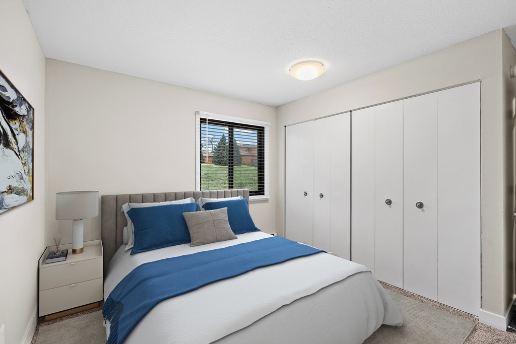 A bedroom with a large bed and a window with blinds.