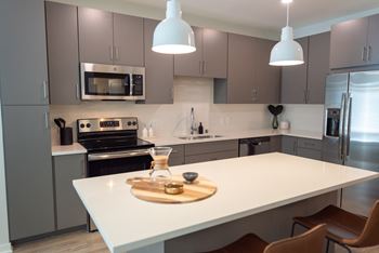 A modern kitchen with a white countertop and brown chairs.