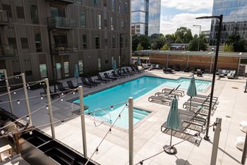 A large swimming pool with lounge chairs and umbrellas on a rooftop patio.