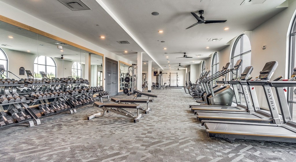 a gym with weights and cardio equipment in a building with windows