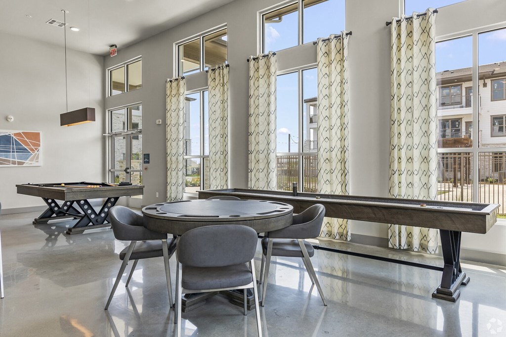 a table with chairs and a shuffleboard table in a room with windows and a pool table