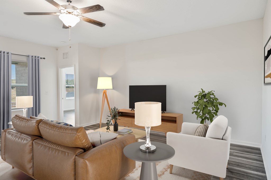 A living room with a brown sofa, a grey table, a black screen, a white chair, and a plant.