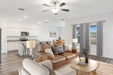 A modern living room with a brown leather couch and a white kitchen in the background.