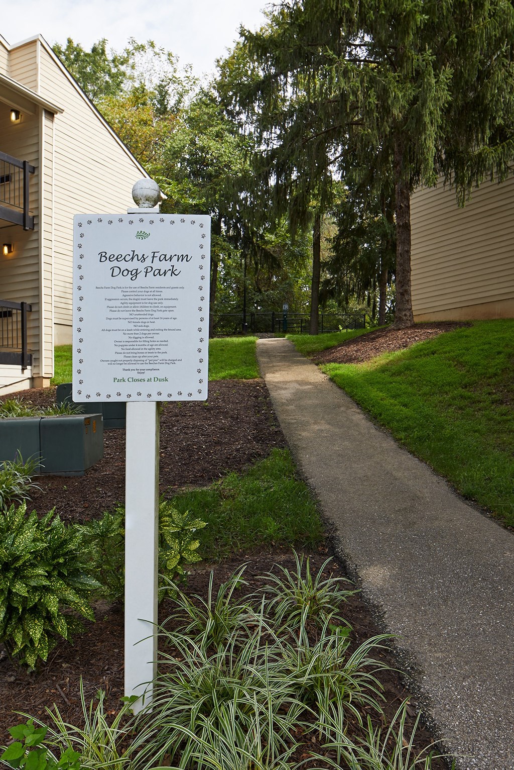 a sign in front of a path with a building and trees