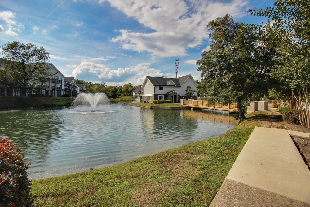 a pond with a fountain and houses on the side of it