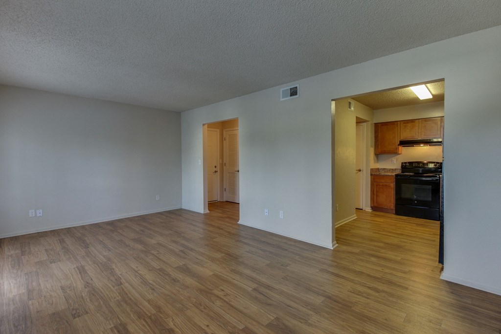 an empty living room with wood floors and a kitchen