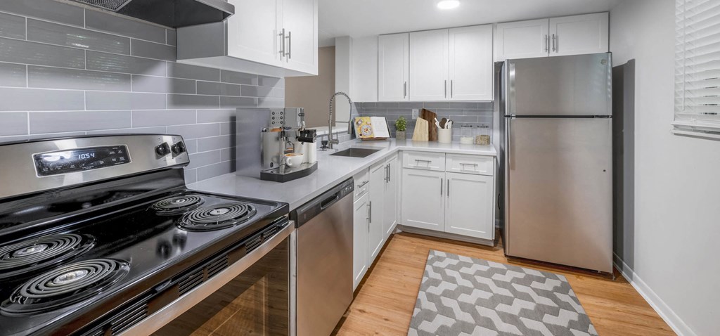 Modern kitchen with stainless steel appliances, white cabinets, gray backsplash, and wood-look flooring.