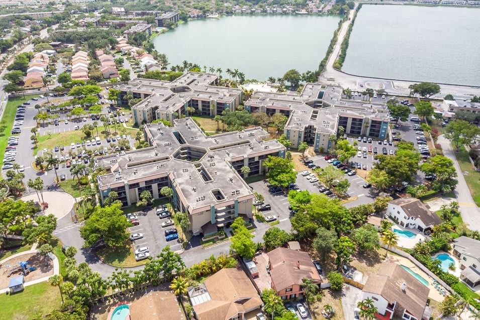 Aerial view of a condominium complex near a lake, surrounded by residential homes and lush greenery.