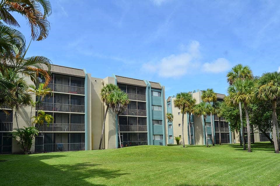 Condominium buildings with balconies surrounded by palm trees and green lawn.