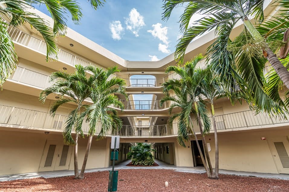 Apartment building courtyard with palm trees and balconies.