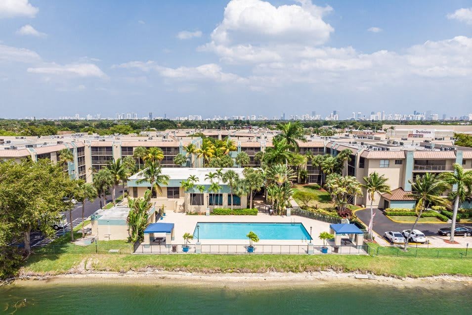 Aerial view of a condominium complex with a swimming pool and distant city skyline.