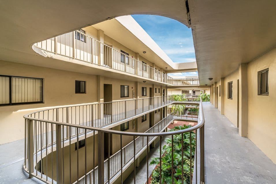 Apartment building courtyard with multiple levels, walkways, and tropical plants.