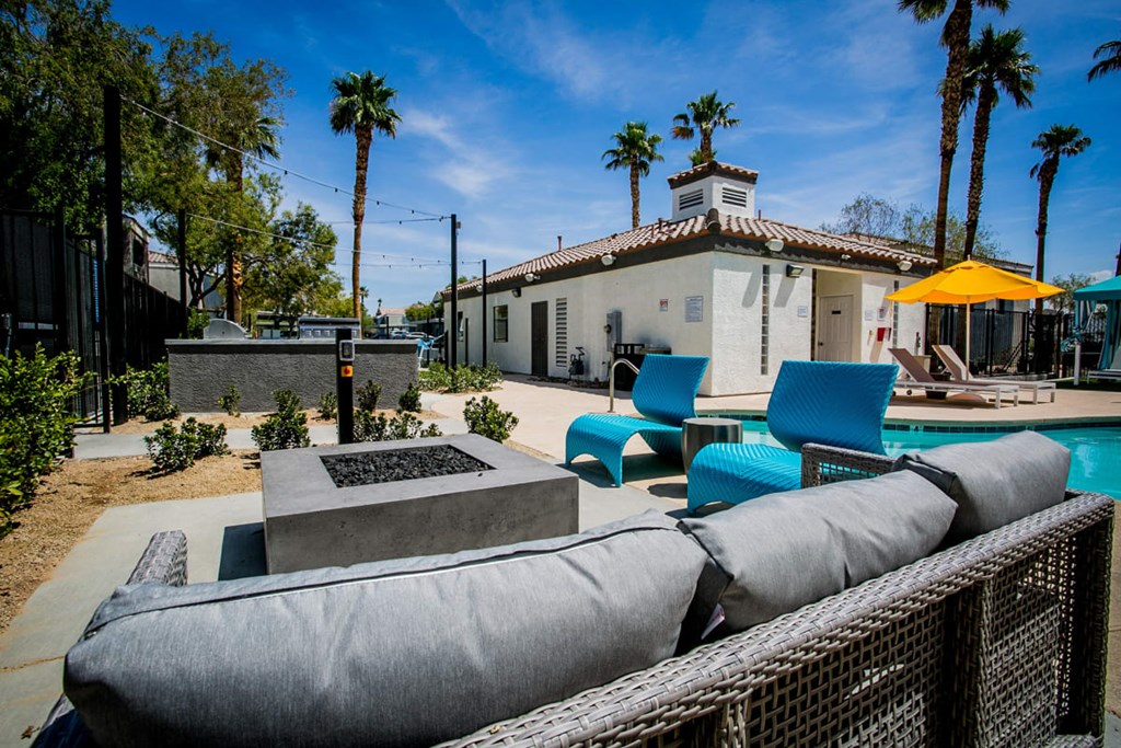 a patio with blue chairs and a fire pit in front of a white house