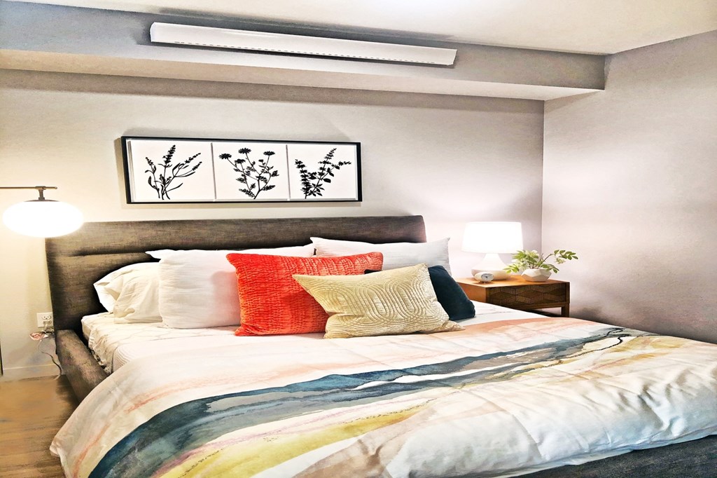 a bedroom with a bed with colorful pillows and a painting on the wall