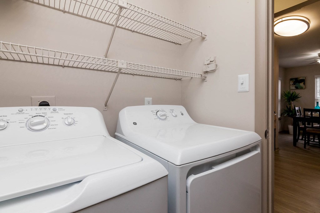 two washers and a dryer in a laundry room with a shelf above them