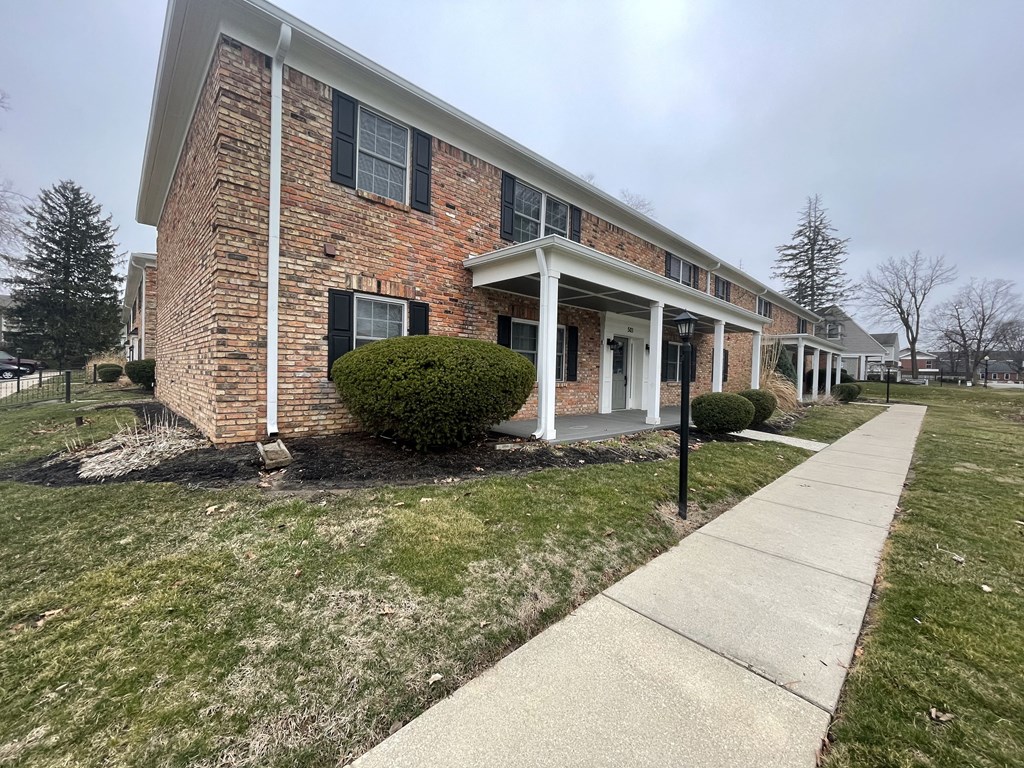 a brick building with a porch and a sidewalk in front of it