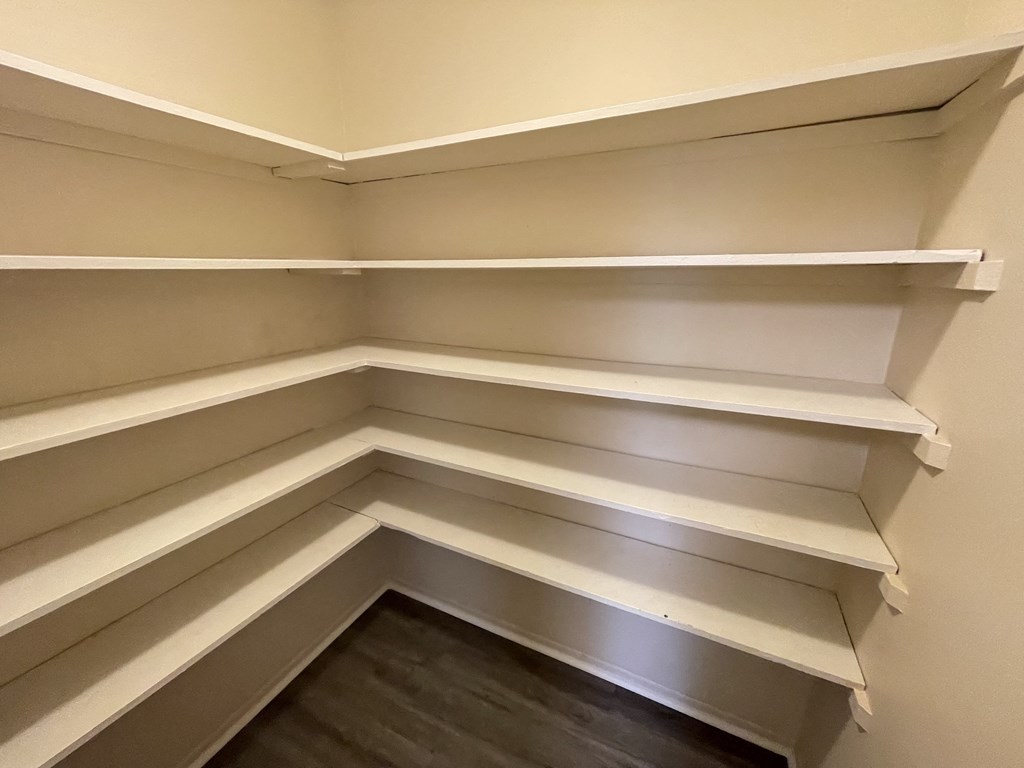 a walk in closet with white shelves and a dark wood floor
