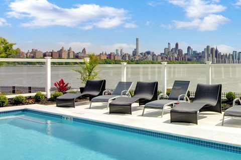 A pool with chairs and a city skyline in the background.