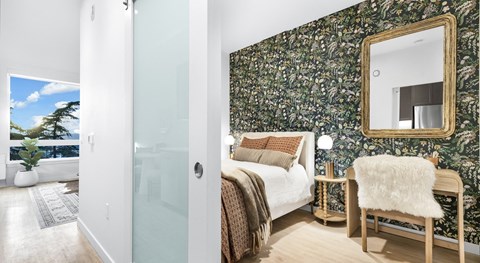 A bedroom with a floral wallpaper and a large mirror above the bed.