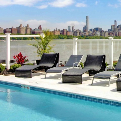 Four black chairs are arranged on a patio next to a pool.