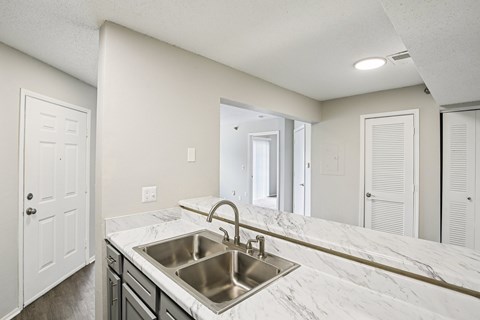 A kitchen with a marble countertop and stainless steel sink.