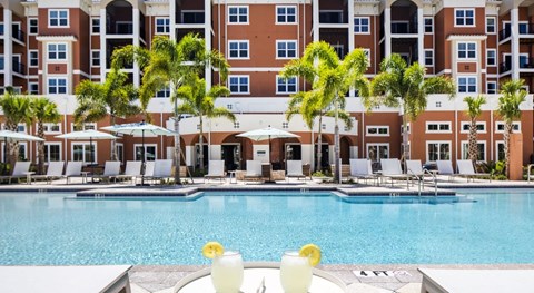 Two drinks are on a table by a pool.