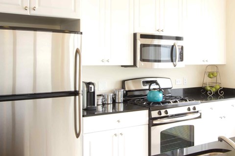 A modern kitchen with a stainless steel refrigerator, a microwave above the stove, and white cabinets.