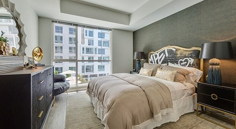 A bedroom with a large bed, a dresser, and a window overlooking a building.