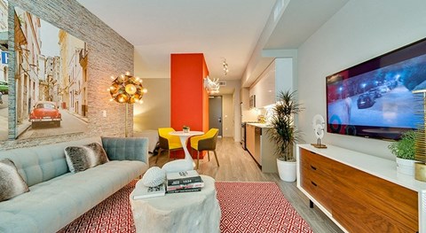 A living room with a white couch, a red rug, and a television on the wall.