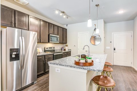A kitchen with a refrigerator, microwave, oven, and sink.