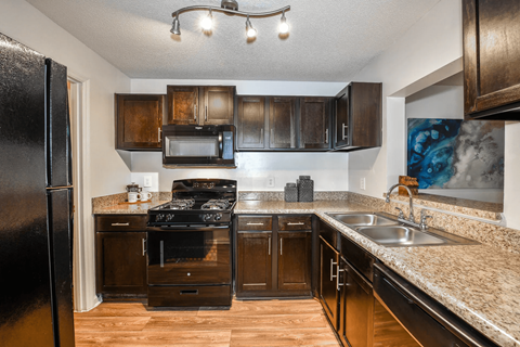A kitchen with a black refrigerator and brown cabinets.