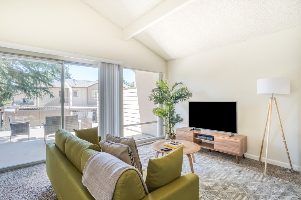 Apartments for Rent in Walnut Creek, CA - Westcliffe Trails - Living Room with a Green Couch, a Flat Screen TV, Carpet Flooring, and a Sliding Glass Door to the Patio/Balcony