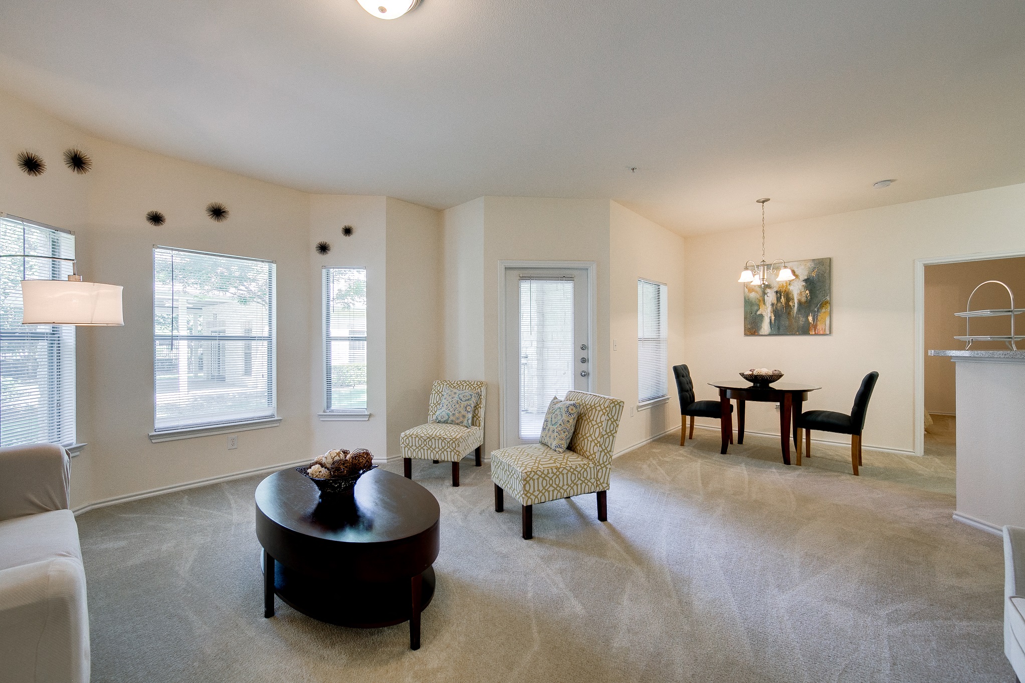 One-Bedroom Apartments in Grand Prairie, TX - Forum at Grand Prairie - Furnished Living Room with High Ceilings, Carpet Flooring, a Dining Area, Many Windows with Blinds, and a Door to the Outside