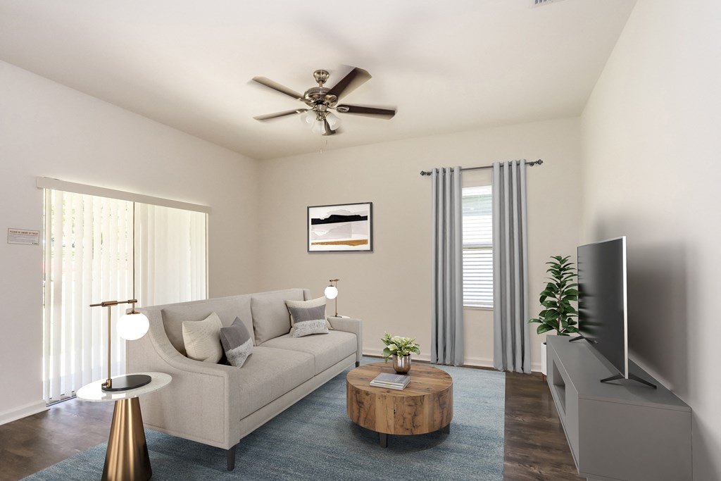 A living room with a beige couch, a coffee table, a television, and a ceiling fan.