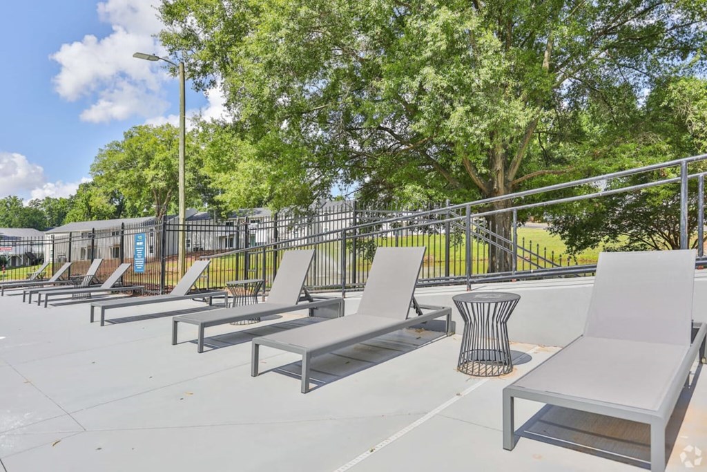 a row of white chaise lounge chairs sit on a concrete patio with trees in the background
