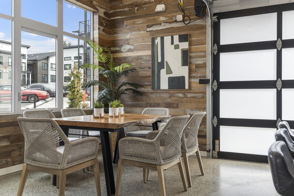 a table and chairs in a room with a wooden wall and large windows,