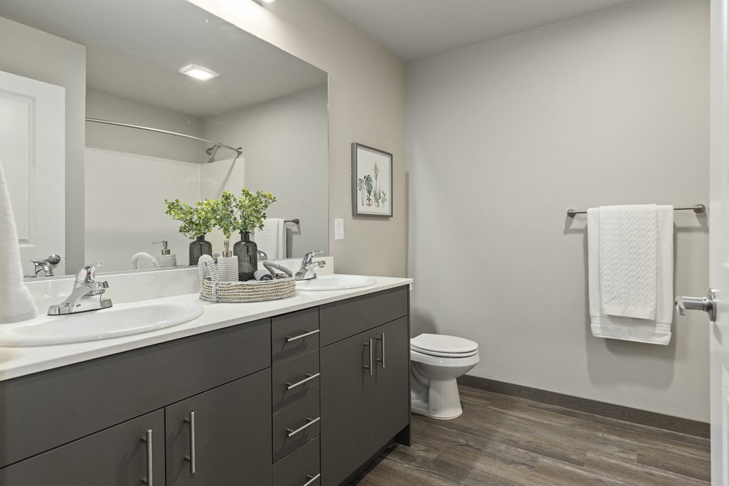 Belfair WA Apartments - Belfair View - a bathroom with a large mirror, dual sink, and wood flooring,