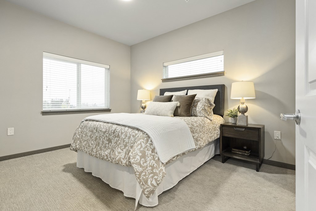 Apartments in Port Orchard, WA for Rent - Belfair View - Bedroom with Carpet Flooring, Bed, Nightstands, Lamps, and Windows.