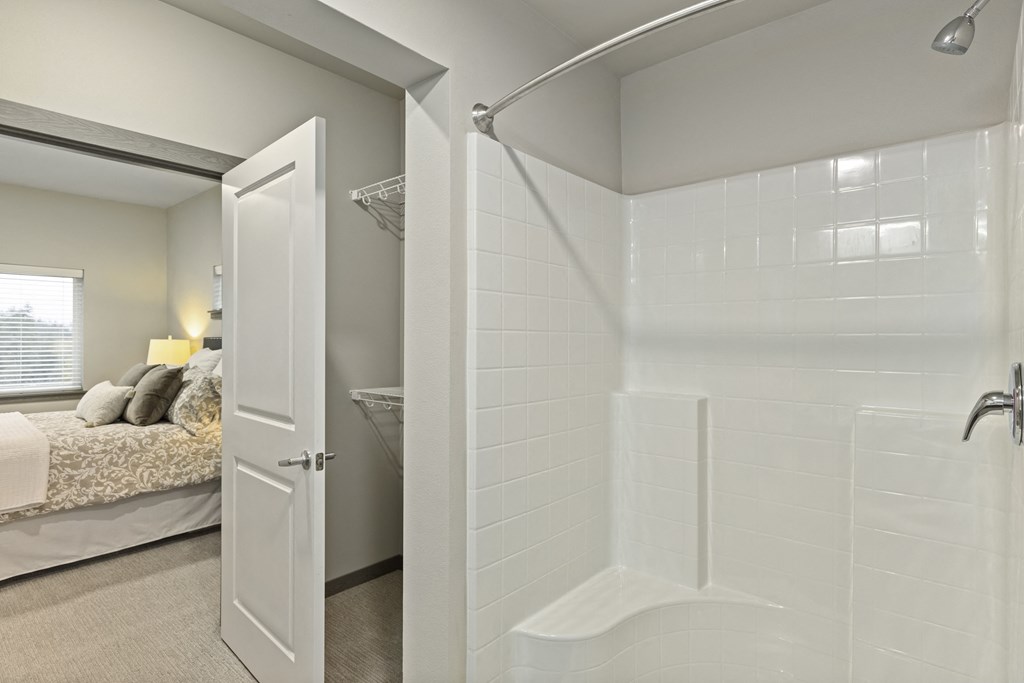 a bathroom with a shower and a bed in the background,